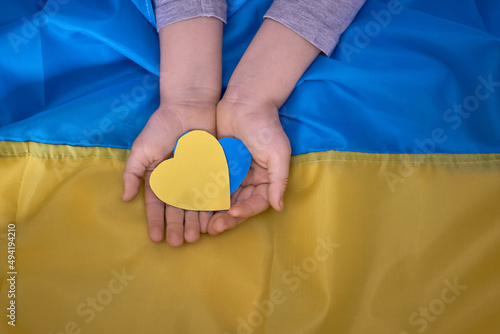 Kids hands holding yellow-blue paperhearts on Ukrainian flag background photo