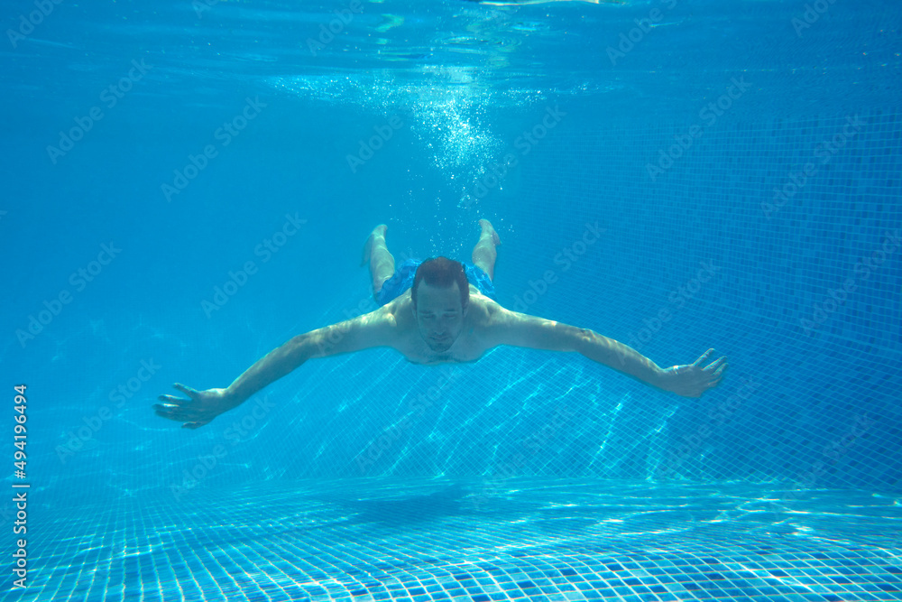 Underwater View Of Man Swimming In Pool On Summer Vacation
