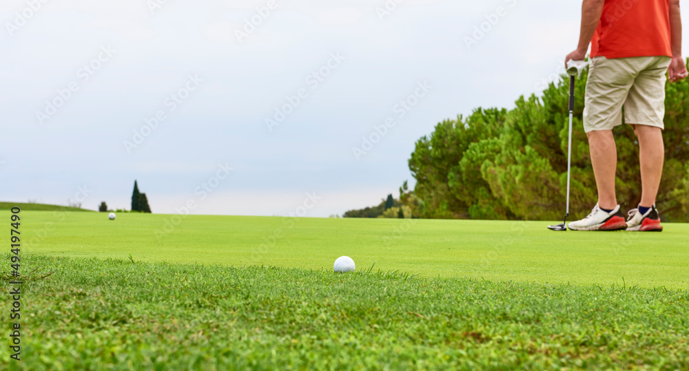 Golfer on the green with a putter in his hands. A player on the green evaluates the slopes and distance from the hole before aiming the ball towards the flag.