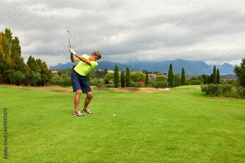 Golfer on a golf course in summer on a day with clouds, hitting the ball with a golf club in the direction of the flag.