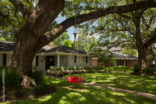 Red tire swing hanging from a tree at the detached residential house garden in Afton Oaks, Houston 