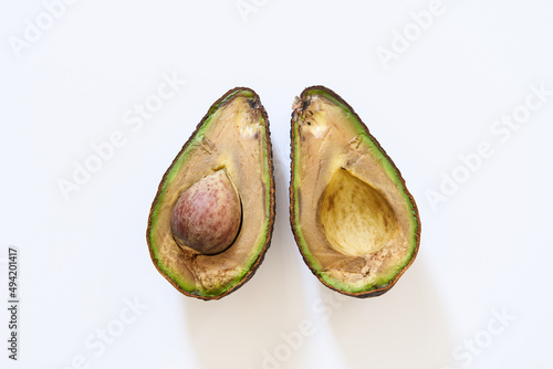 A rotten avocado on a white background. The overripe avocado is cut in half. The core is in the fruit.