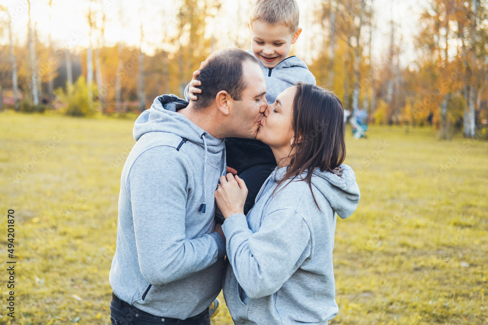 Parents with their son are walking in the park having fun, smiling and kissing. Adoption kid. Happy people. Summer vacation. Family care. Parents with their son are walking in the park having fun, smiling and kissing. Adoption kid. Happy people. Summer vacation. Family care.