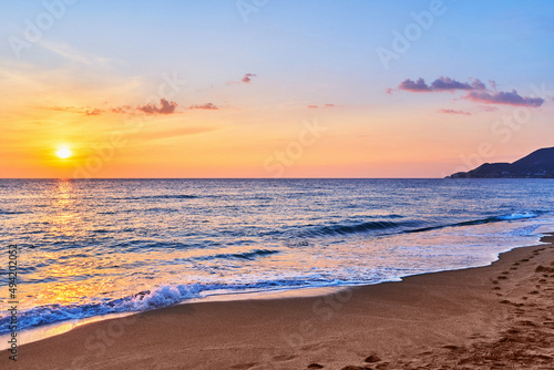Landscape of scenic idyllic peaceful calm sky wallpaper with sea waves coast and sandy beach at golden sunset © Goffkein