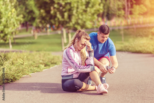 Young woman with knee injury while jogging outdoor helped by her male partner
