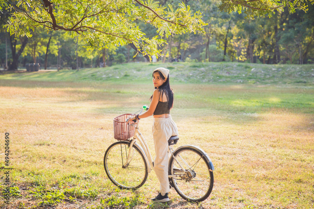 Obraz premium Portrait Asian woman in a green singlet sitting on a bicycle on a lawn with nature background in a park