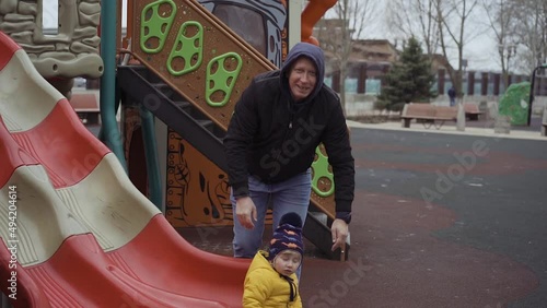 Father with adorable little son playing on slide in the park