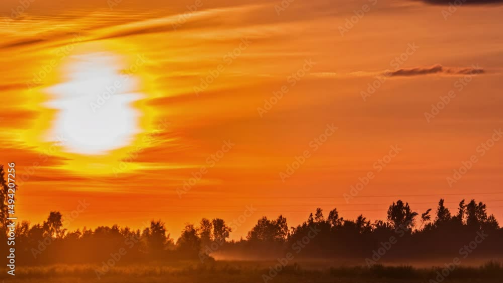 Static view of sunset in timelapse over the green grasslands. Dramatic sunset sky red yellow cloudy sun setting over sky. Static view of sunset in timelapse over the green grasslands. Dramatic sunset sky red yellow cloudy sun setting over sky.