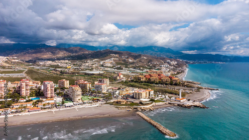 Drone perspective of costal city of Torrox situated in Malaga, Costa del Sol, Spain. Touristic travel destination. View of the promenade and beach area. The lighthouse of Torrox and the river.