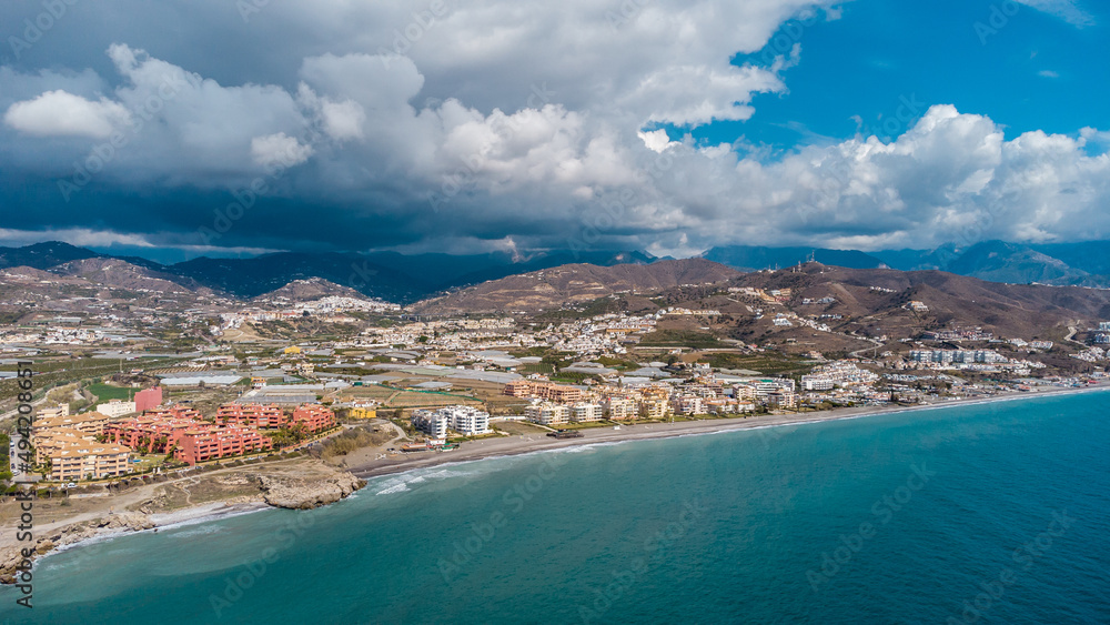 Drone perspective of costal city of Torrox situated in Malaga, Costa del Sol, Spain. Touristic travel destination. View of the promenade and beach area. The lighthouse of Torrox and the river.