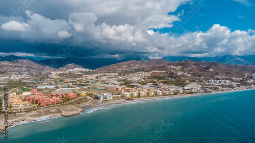 Drone perspective of costal city of Torrox situated in Malaga, Costa del Sol, Spain. Touristic travel destination. View of the promenade and beach area. The lighthouse of Torrox and the river.