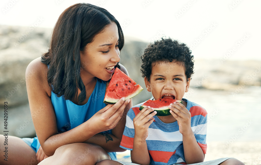 Watermelon is out favourite fruit. Shot of a mother and sitting down and enjoying some watermelon at the beach.