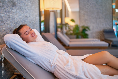 Obraz na plátně Carefree satisfied serene female with hands behind head lying on chaise longue chilling and relaxing alone in spa center