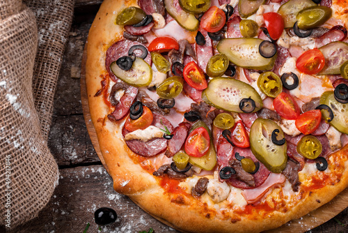 pizza with salami barbecue sausages ham tomatoes bell peppers on a wooden board sprinkled with flour