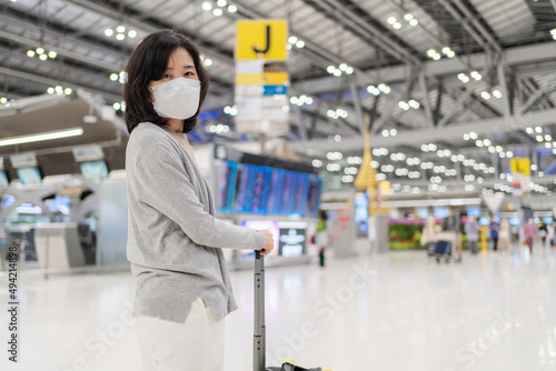 Woman with luggage standing in the international airport terminal wearing hygiene face mask to prevent Covid 19 outbreak. Waiting for check in before go aboard. Transportation and new normal concept