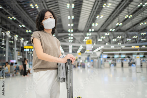 Woman with luggage standing in the international airport terminal wearing hygiene face mask to prevent Covid 19 outbreak. Waiting for check in before go aboard. Transportation and new normal concept