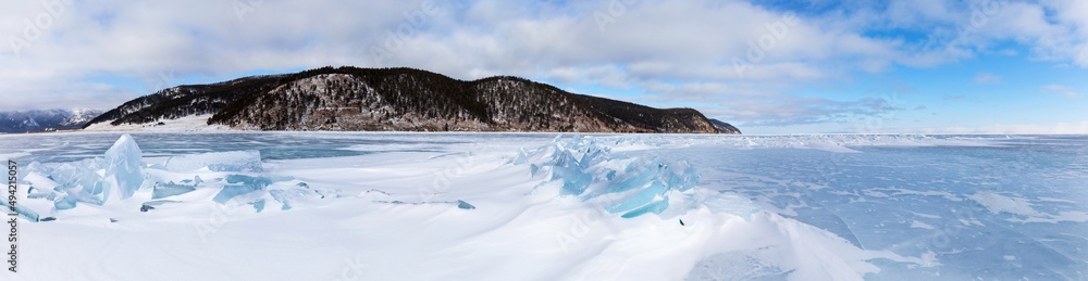 Panoramic view of coast of frozen Baikal Lake near Bolshoe Goloustnoye village. Beautiful winter landscape with snowy surface of blue ice with ice hummocks on cold January day. Natural background Panoramic view of coast of frozen Baikal Lake near Bolshoe Goloustnoye village. Beautiful winter landscape with snowy surface of blue ice with ice hummocks on cold January day. Natural background