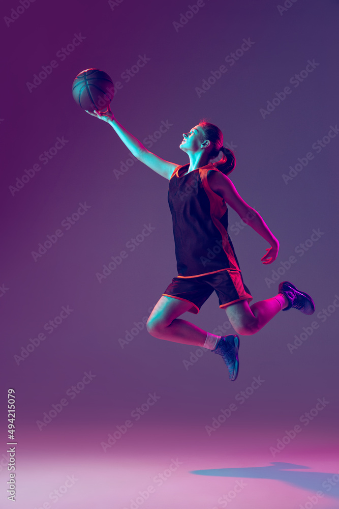 Portrait of young active girl, professional basketball player training isolated over gradient pink purple background in neon