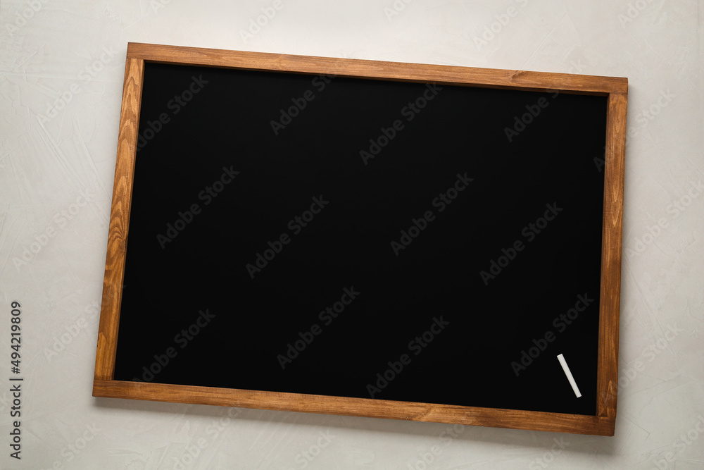 Clean blackboard with piece of chalk on light table, top view