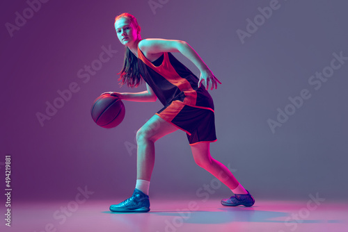 Portrait of young girl, teen, basketball player in motion, training isolated over gradient pink purple background in neon © master1305