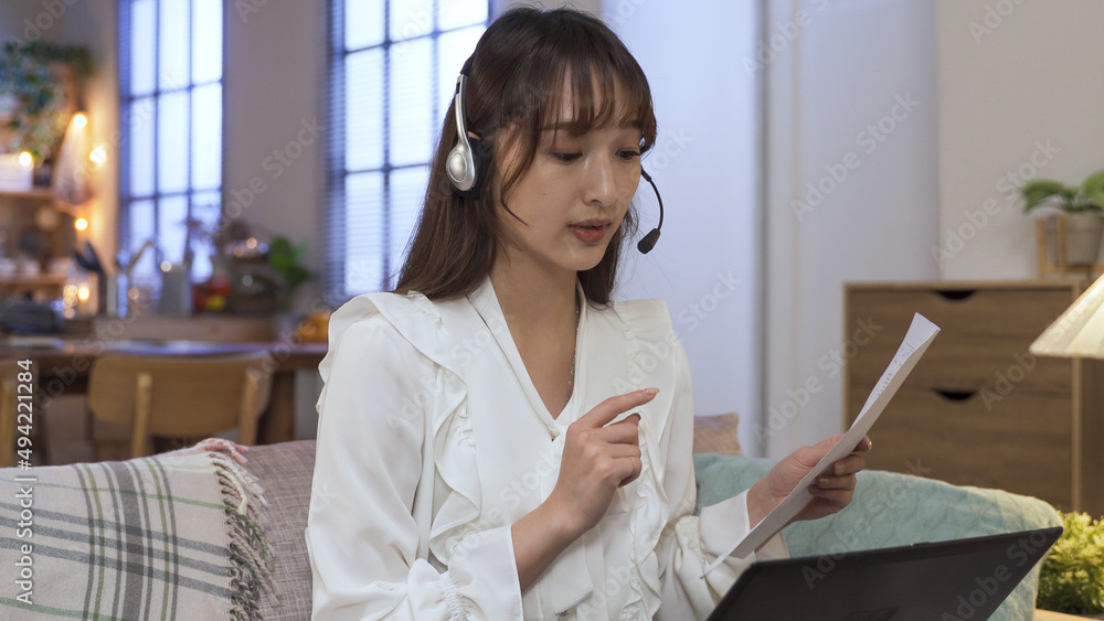 woman with headphones and document is making hand gestures while reporting her project in a conference call. working from home with modern technology during virus outbreak.