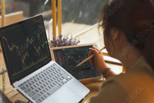 Asian Businesswoman, female trader, investor using laptop, tablet for stock market, Bitcoin cryptocurrency trading, strategy planning on money investing on online trading platform. Trading concept.
