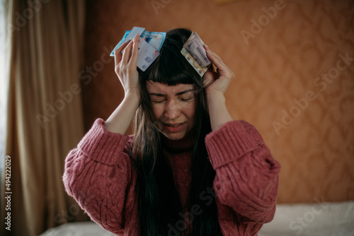 A woman frustratedly holds her head, holds in her hands the currency of different countries and bank cards. Concept of crisis photo