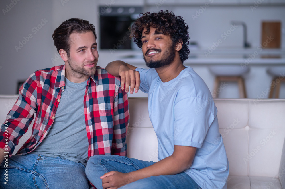 Fototapeta premium Romantic biracial gay couple sitting on the sofa