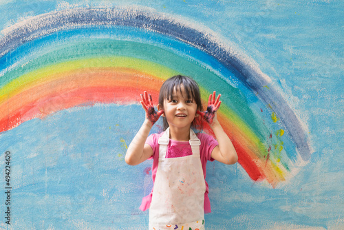 Asian little girl is painting the colorful rainbow and sky on the wall and she look happy and funny, concept of art education and learn through play activity for kid development.