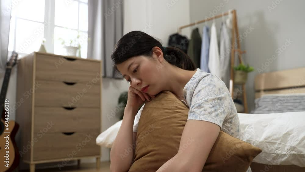 closeup shot unhappy asian young woman holding a pillow and staring into space while experiencing depression during quarantine in the bedroom at home. closeup shot unhappy asian young woman holding a pillow and staring into space while experiencing depression during quarantine in the bedroom at home.