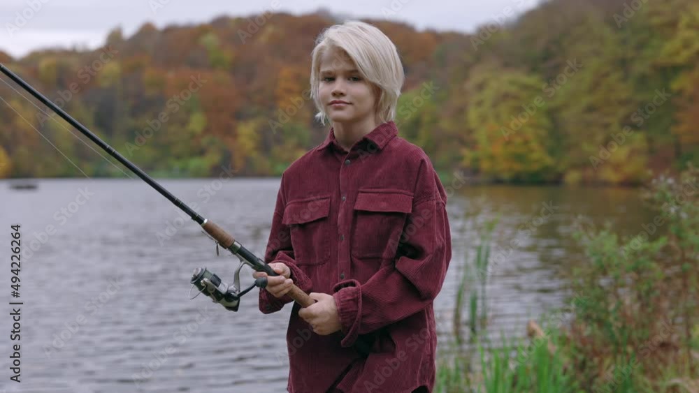 Teen boy holding fishing rod while standing on riverside Teen boy holding fishing rod while standing on riverside