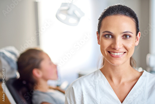 So glad I decided to specialize in dentistry. A female dentist standing in her office with her child patient in the background.