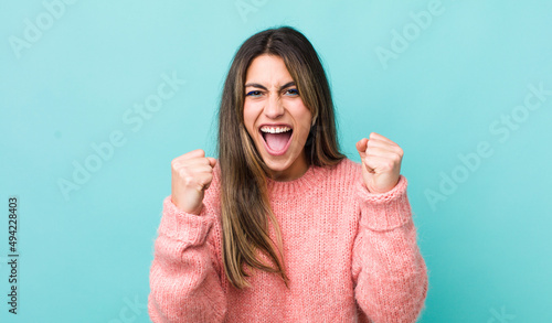 pretty hispanic woman feeling happy, positive and successful, celebrating victory, achievements or good luck