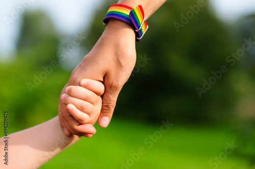 parent holds the hand of a small child. mother holding baby's hand. rainbow lgbt bracelet on parents hand