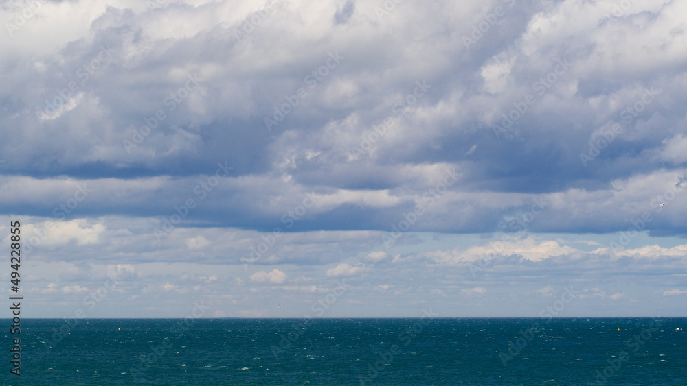 Vue en paysage, sur la Mer Méditerranée.  Le ciel est partiellement couvert par des cumulus de beau temps