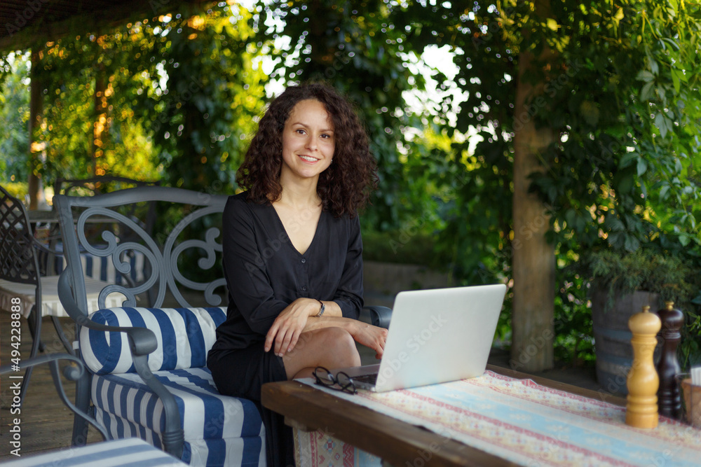 Cheerful young woman working on laptop computer while sitting at the terrace, looking at camera. Cheerful young woman working on laptop computer while sitting at the terrace, looking at camera.