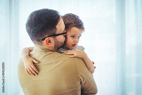 Father comforting stressed sad son. Close up of  father consoling his small sad son at home. Small boy crying in his father's hug at home. © Dragana Gordic