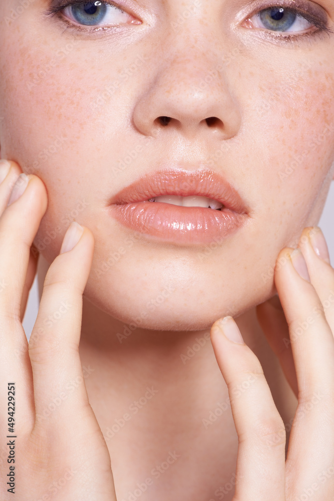 Lightly freckled and beautiful. Cropped close up of a young woman touching her face.