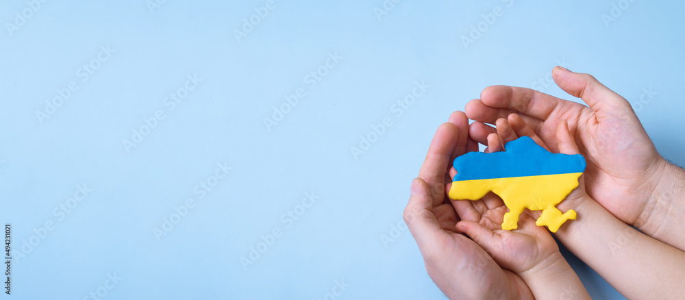 Shape of the map of Ukraine in yellow and blue colors in the hands of an adult and a child. Banner with copy space Shape of the map of Ukraine in yellow and blue colors in the hands of an adult and a child. Banner with copy space