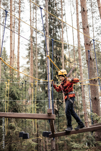 Teenager boy in safety equipment routing and climbing in adventure rope park. Child in helmet climbing trees in an extreme park. Outdoor activities. Active lifestyle