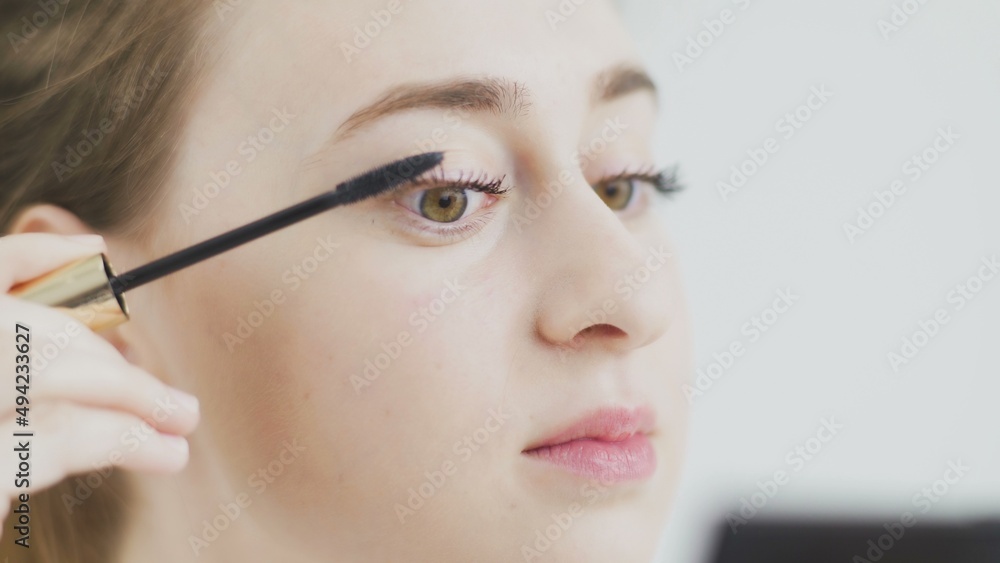 Make-up on the face. Close-up of a young woman painting her long eyelashes with black mascara.