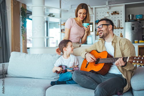 Single Father At Home With Son Teaching Him To Play Acoustic Guitar at home. Getting it right together. Shot of a boy learning to play guitar from his father