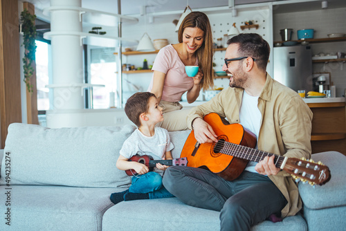 Father teaching his son to play on guitar at home. Son play on ukulele - hawaiian guitar. Father is teaching his 5 year old son to play guitar. First guitar class