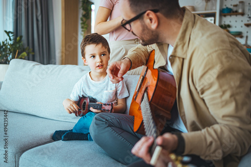 Father At Home With Son Teaching Him To Play Acoustic Guitar In Livingroom. First guitar class. Shot of a boy learning to play guitar from his father