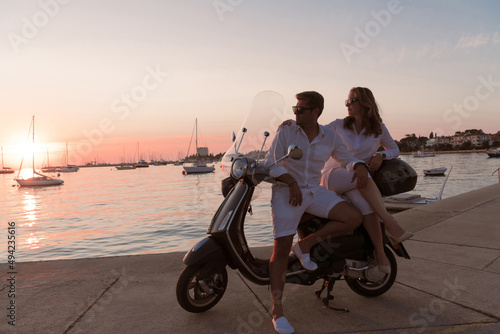 The couple enjoys a vacation while sitting on a scooter by the sea and enjoying the beautiful sunrise. Selective focus 