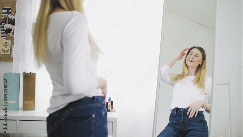 A young woman looks in the mirror, preens herself, admires herself, corrects her clothes and hairstyle. He smiles and likes himself. A young woman looks in the mirror, preens herself, admires herself, corrects her clothes and hairstyle. He smiles and likes himself.