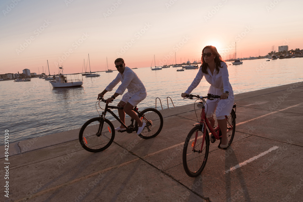 Fototapeta premium Happy family enjoying a beautiful morning by the sea together, parents riding a bike and their son riding an electric scooter. Selective focus