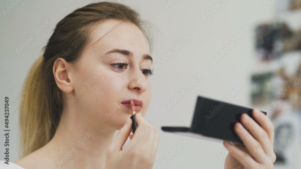 The girl paints her lips with lipstick. Close-up of the face. Macro photography of A Woman Wearing lipstick. The face macro. The girl looks in a small mirror