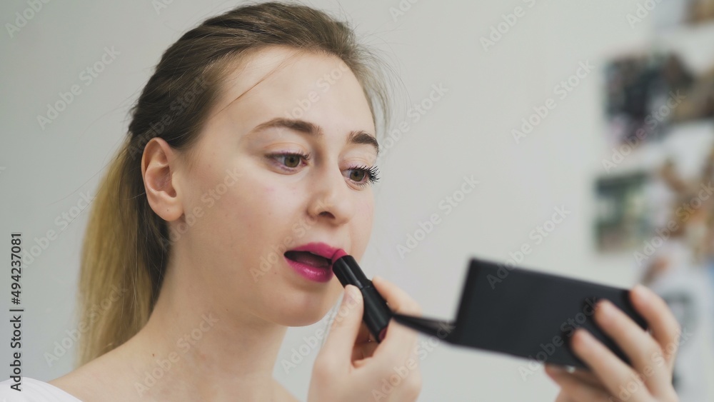 The girl paints her lips with lipstick. Close-up of the face. Macro photography of A Woman Wearing lipstick. The face macro. The girl looks in a small mirror The girl paints her lips with lipstick. Close-up of the face. Macro photography of A Woman Wearing lipstick. The face macro. The girl looks in a small mirror