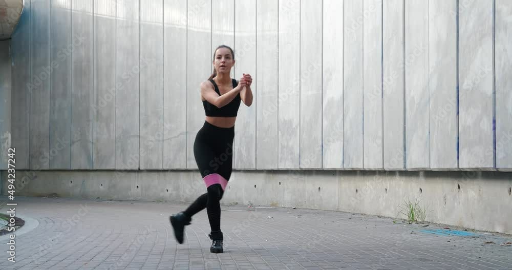 Beautiful fitness young woman in sporty tight squatting using rubber band resistance. Female workout with rubber elastic band outdoors Beautiful fitness young woman in sporty tight squatting using rubber band resistance. Female workout with rubber elastic band outdoors